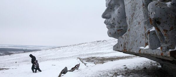A man and a child walk in the snow at the destroyed war memorial at Savur-Mohyla, a hill east of the city of Donetsk - Sputnik International