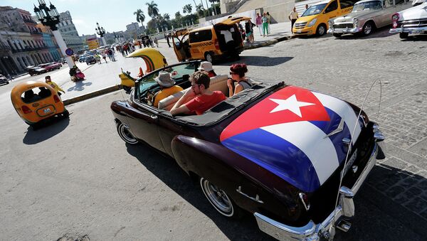 Tourists take a ride in a classic American convertible car with the Cuban national flag - Sputnik International