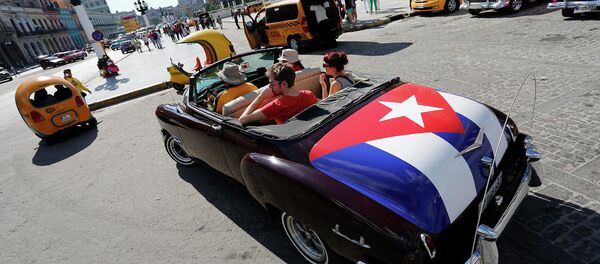 Tourists take a ride in a classic American convertible car with the Cuban national flag - Sputnik International