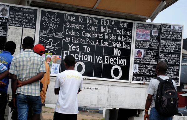 Bystanders read the headlines illustrating the battle over the holding of elections in Liberia amid the Ebola crisis at a street side chalkboard newspaper in Monrovia. (File) - Sputnik International