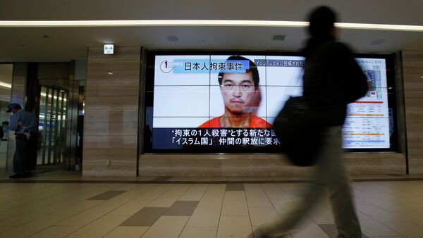A man walks past screens displaying a television news programme showing an image of Kenji Goto, one of two Japanese citizens taken captive by Islamic State militants, on a street in Tokyo January 25, 2015 - Sputnik International