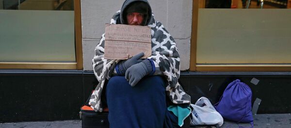 A man holding up a sign stating he is 'homeless, hungry and cold' sits along 7th avenue in New York - Sputnik International