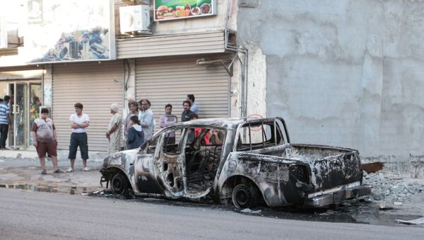 Men stand near a burned vehicle in the eastern town of al-Awamiya, Saudi Arabia - Sputnik International