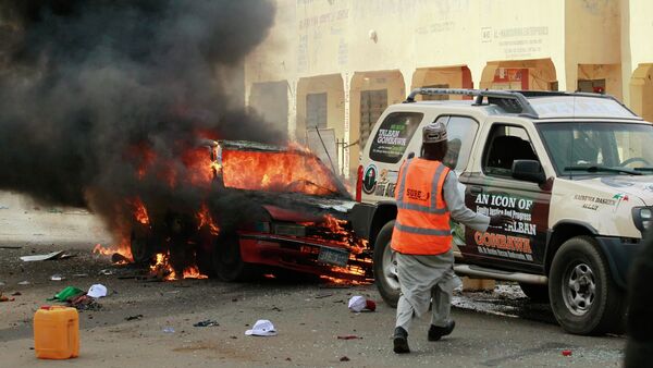 A man rushes towards a vehicle next to a burning car at the scene of a bomb explosion in Gombe - Sputnik International