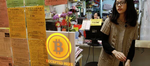 A staff member from a travel agency displays a Bitcoin logo as they accept bitcoins for payment in Hong Kong Friday, Feb. 28, 2014, after the world's first bitcoin retail store opened in Hong Kong, despite the virtual currency facing much scrutiny. - Sputnik International