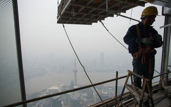 A worker installs wires on the 109th floor of the Shanghai Tower (still under construction) in front of the smog covered skyline of the Lujiazui Financial District in Shanghai on October 16, 2014 - Sputnik International