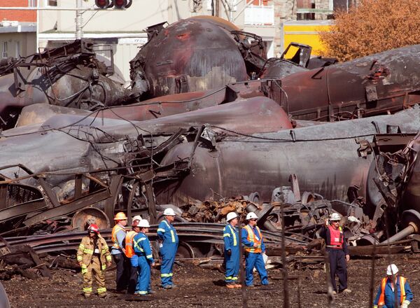 In this July 6, 2013, file photo, workers stand before mangled tanker cars at the crash site of the train derailment and fire in Lac-Megantic, Quebec, Canada. In this July 6, 2013, file photo, workers stand before mangled tanker cars at the crash site of the train derailment and fire in Lac-Megantic, Quebec, Canada. - Sputnik International