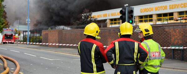 Firefighters stand beside a cordon as they tend to a fire at a recycling plant in Smethwick near Birmingham Firefighters stand beside a cordon as they tend to a fire at a recycling plant in Smethwick near Birmingham - Sputnik International