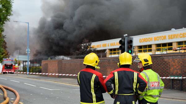 Firefighters stand beside a cordon as they tend to a fire at a recycling plant in Smethwick near Birmingham - Sputnik International