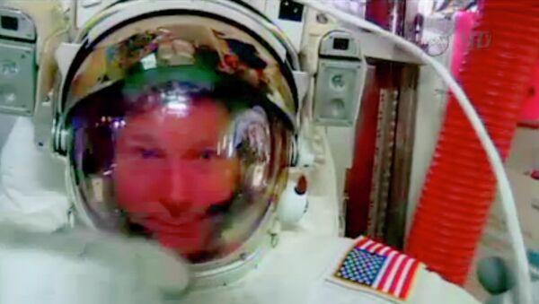 In this screenshot from a video provided by NASA, astronaut Terry Virts points to his helmet as he sits inside the International Space Station Wednesday during an inspection for water in his suit. - Sputnik International