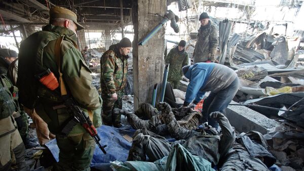 Independent supporter stand next to bodies of Ukrainian servicemen retrieved from the rubble of the airport building a man searches them for identity papers outside Donetsk - Sputnik International