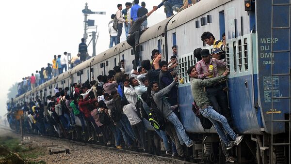 Indian passengers stand and hang onto a train as it departs from a station on the outskirts of New Delhi on February 25, 2015 - Sputnik International