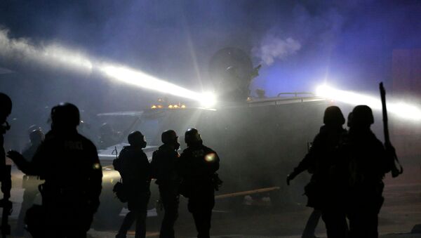 Police in riot gear stand around an armored vehicle as smoke fills the streets Tuesday, Nov. 25, 2014, in Ferguson, Mo. - Sputnik International