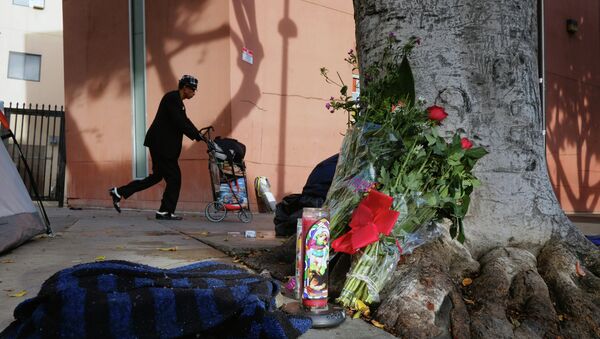 A pedestrian walks past flowers and candles placed on a sidewalk near where a man was shot and killed by police in the Skid Row section of downtown Los Angeles - Sputnik International