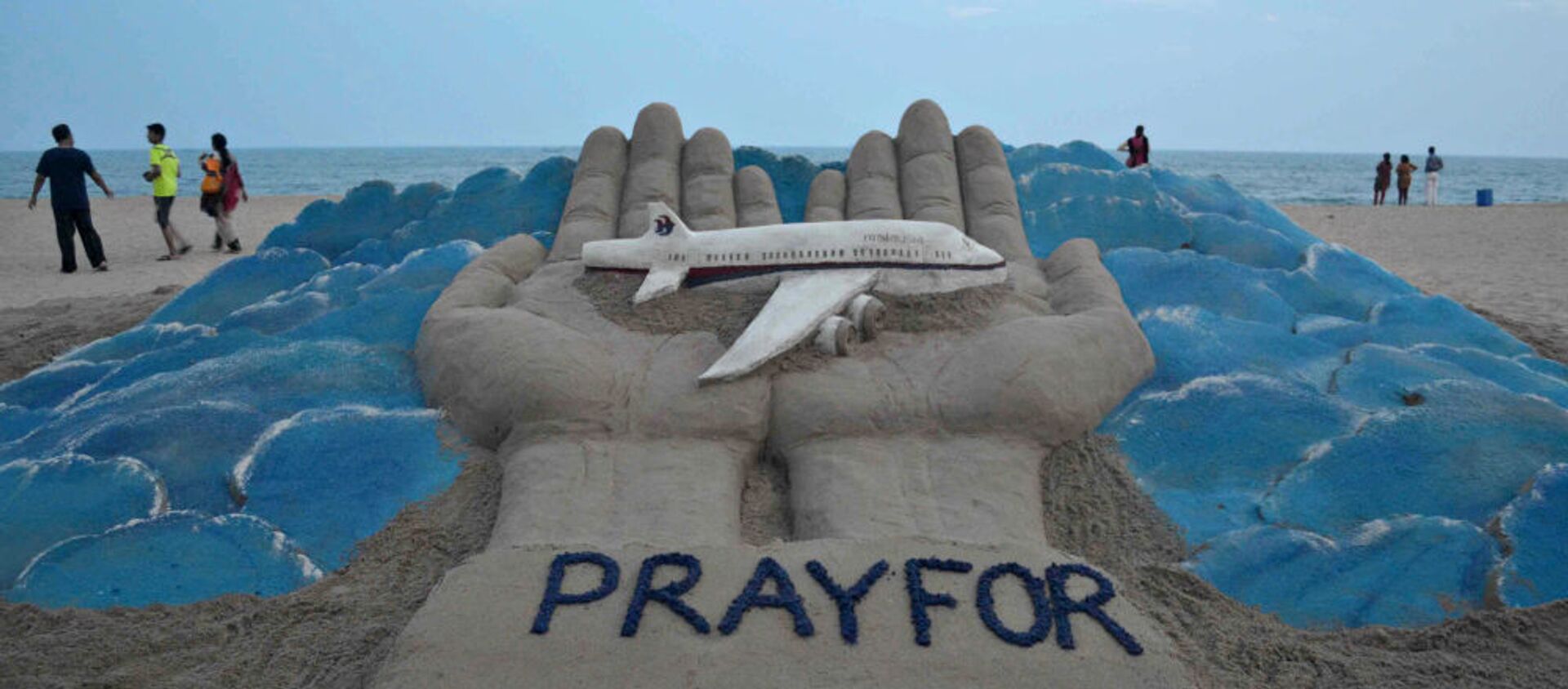 Beachgoers walk past a sand sculpture made by Indian sand artist Sudersan Pattnaik with a message of prayers for the missing Malaysian Airlines flight MH370 - Sputnik International, 1920, 06.05.2021