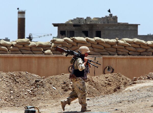 A Kurdish Peshmerga fighter carries his weapon walks onto his base, where two flags of the Islamic State in Iraq and the Levant (ISIL) are seen on a building, right, and water tower, left, at the front line with the al-Qaida-inspired militants in Tuz Khormato, 100 kilometers (62 miles) south of the oil rich province of Kirkuk, northern Iraq.  - Sputnik International