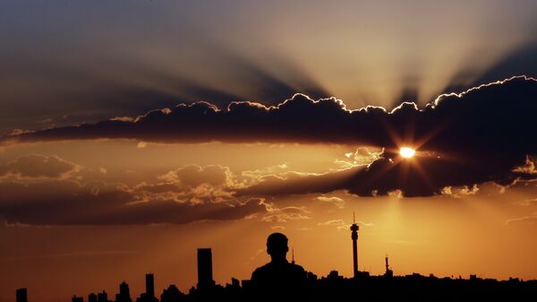 A man watches the sun set in as he overlooks the skyline in Johannesburg, South Africa - Sputnik International