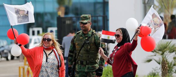 Egyptian women wave flags with pictures of Egyptian President Abdel Fattah al-Sisi, next to a soldier outside a conference centre hosting the Egypt Economic Development Conference (EEDC) in Sharm el-Sheikh, in the South Sinai governorate, south of Cairo, March 14, 2015 - Sputnik International