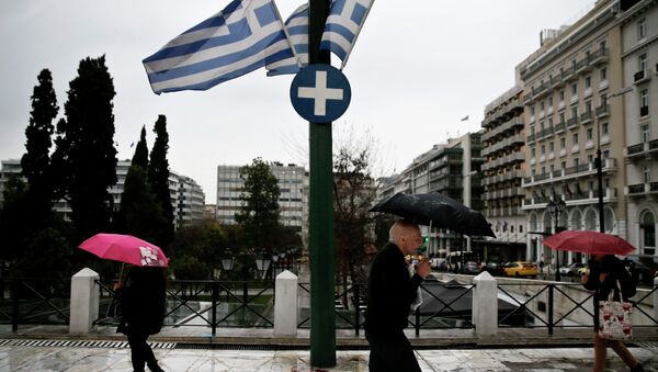 People holding umbrellas make their way next to fluttering Greek national flags on the main Constitution (Syntagma) square during heavy rainfall in Athens - Sputnik International