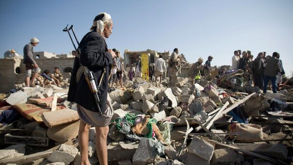 A Houthi Shiite fighter stand guard as people search for survivors under the rubble of houses destroyed by Saudi airstrikes near Sanaa Airport, Yemen - Sputnik International