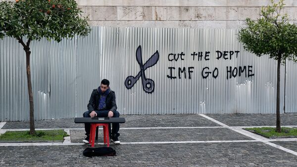 A man plays music on a digital keyboard near graffiti on a corrugated metal gate reading Cut the debt, IMF go home in Athens on February 24, 2015 - Sputnik International