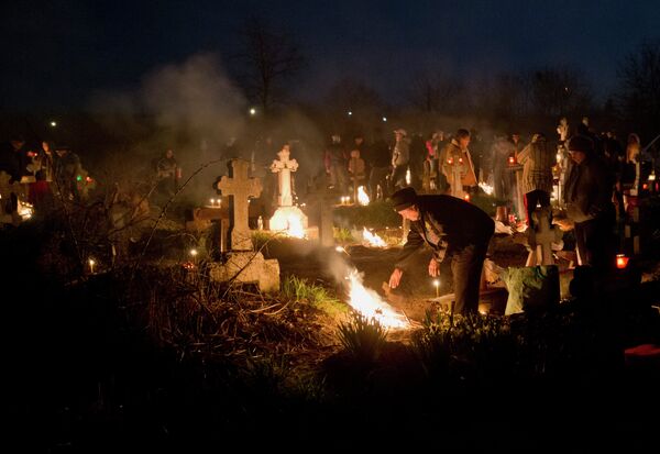 People stand by fires they lit by a relative's grave in a cemetery during an Orthodox Palm Sunday memorial for the departed in Herasti, southern Romania, early Sunday, April 5, 2015 - Sputnik International