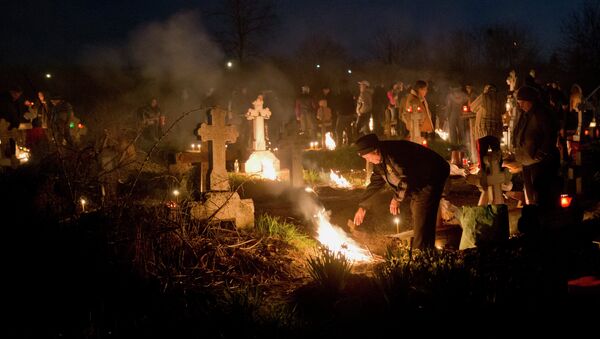 People stand by fires they lit by a relative's grave in a cemetery during an Orthodox Palm Sunday memorial for the departed in Herasti, southern Romania, early Sunday, April 5, 2015 - Sputnik International