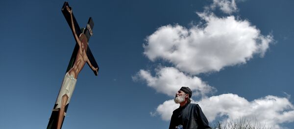 A monk of the Greek Orthodox Church looks at an image of Jesus crucified during the ceremony marking the Apokathelosis, the removal of Christ's dead body from the Cross, which forms a key part of Orthodox Easter, in a ceremony at the Church of the Dormition of the Virgin in Penteli, north Athens - Sputnik International