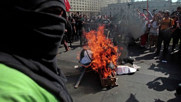 A masked demonstrator stands next to a pile of debris set on fire during a protest near La Moneda Palace in Santiago, Chile, Thursday, April 16, 2015. Thousands of students marched through the streets of Chile’s capital to protest recent corruption scandals and to complain about delays in a promised education overhaul. While it was largely peaceful, violence broke out at the end when hooded protesters threw rocks and gasoline bombs at police. At least one officer was injured. - Sputnik International