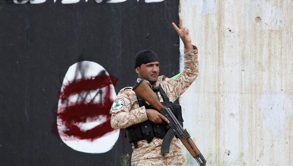 A member of the Iraqi security forces flashes the sign for victory in front of a defaced Islamist flag in Tikrit - Sputnik International