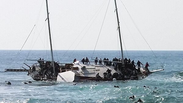 Migrants, who are trying to reach Greece, are seen onboard a capsized sailboat, as others are seen in the water trying to reach the coast of the southeastern island of Rhodes April 20, 2015 - Sputnik International