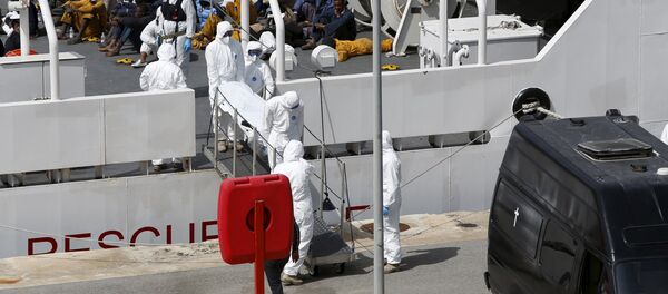 Armed Forces of Malta personnel in protective clothing carry the body of a dead immigrant off Italian coastguard ship Bruno Gregoretti as surviving migrants watch in Senglea, in Valletta's Grand Harbour, April 20, 2015 Armed Forces of Malta personnel in protective clothing carry the body of a dead immigrant off Italian coastguard ship Bruno Gregoretti as surviving migrants watch in Senglea, in Valletta's Grand Harbour, April 20, 2015 - Sputnik International