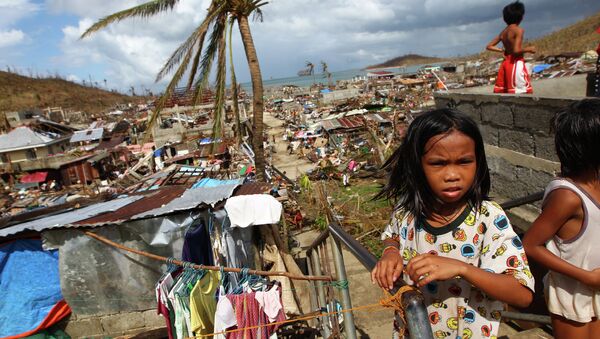 Filipino children play as houses damaged by Typhoon Haiyan are seen in the background in Marabut, Philippines in 2013. - Sputnik International