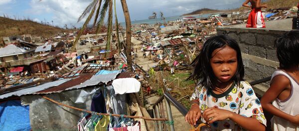 Filipino children play as houses damaged by Typhoon Haiyan are seen in the background in Marabut, Philippines in 2013. - Sputnik International