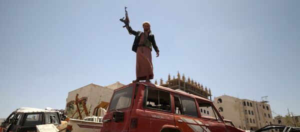 A follower of the Houthi group raises his weapon as he stands on a vehicle on a damaged street, caused by an April 20 air strike that hit a nearby army weapons depot, in Sanaa April 21, 2015 - Sputnik International