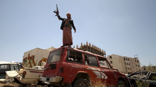 A follower of the Houthi group raises his weapon as he stands on a vehicle on a damaged street, caused by an April 20 air strike that hit a nearby army weapons depot, in Sanaa April 21, 2015 - Sputnik International