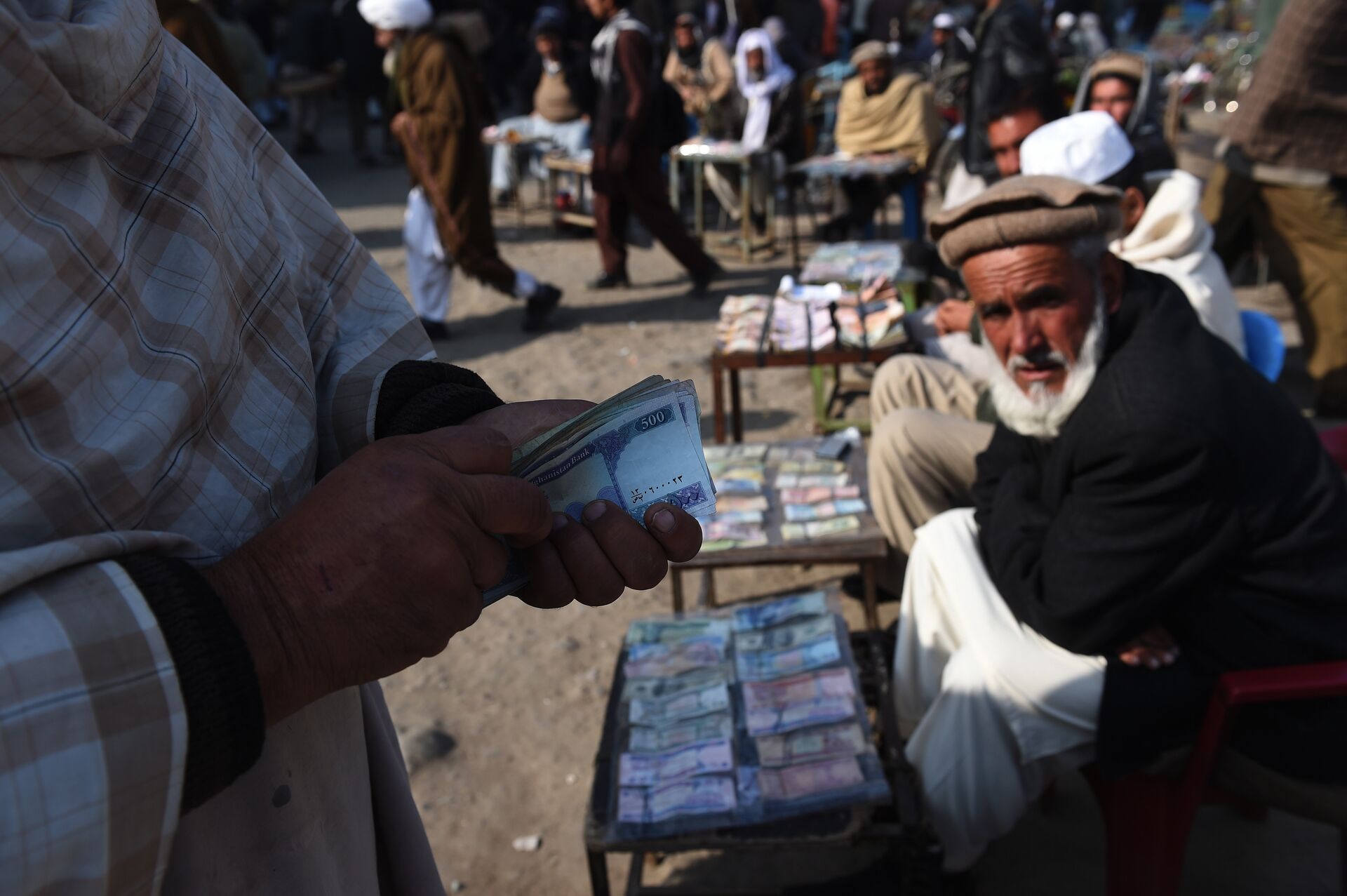 In this photograph taken on December 29, 2014, an Afghan customer (L) counts his Afghani currency notes at a currency exchange market along the roadside in Kabul - Sputnik International, 1920, 23.02.2022