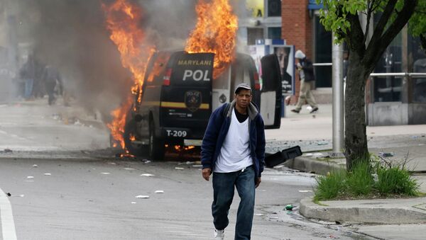 A man walks past a burning police vehicle, Monday, April 27, 2015, during unrest following the funeral of Freddie Gray in Baltimore. Gray died from spinal injuries about a week after he was arrested and transported in a Baltimore Police Department van. - Sputnik International