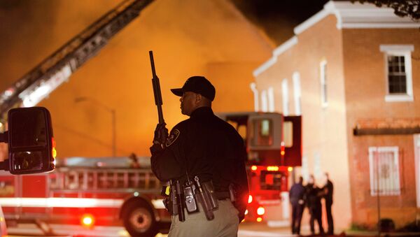 An officer stands near a blaze, Monday, April 27, 2015, after rioters plunged part of Baltimore into chaos, torching a pharmacy, setting police cars ablaze and throwing bricks at officers. - Sputnik International