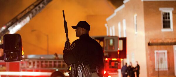 An officer stands near a blaze, Monday, April 27, 2015, after rioters plunged part of Baltimore into chaos, torching a pharmacy, setting police cars ablaze and throwing bricks at officers. - Sputnik International