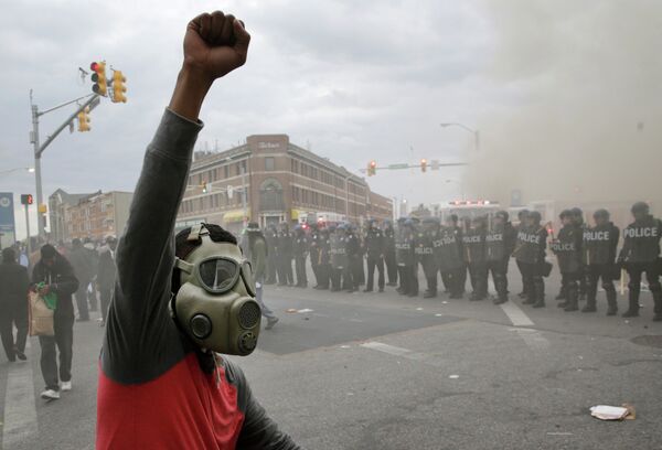 A demonstrator raises his fist as police stand in formation as a store burns, Monday, April 27, 2015, during unrest following the funeral of Freddie Gray in Baltimore A demonstrator raises his fist as police stand in formation as a store burns, Monday, April 27, 2015, during unrest following the funeral of Freddie Gray in Baltimore - Sputnik International