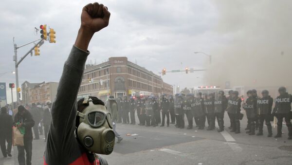A demonstrator raises his fist as police stand in formation as a store burns, Monday, April 27, 2015, during unrest following the funeral of Freddie Gray in Baltimore - Sputnik International