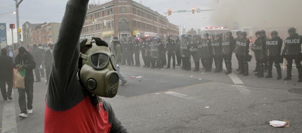A demonstrator raises his fist as police stand in formation as a store burns, Monday, April 27, 2015, during unrest following the funeral of Freddie Gray in Baltimore A demonstrator raises his fist as police stand in formation as a store burns, Monday, April 27, 2015, during unrest following the funeral of Freddie Gray in Baltimore - Sputnik International