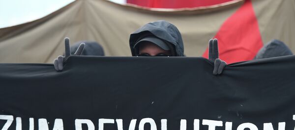 A protester shows the victory sign as he marches with a banner promoting a social revolution worldwide as he takes part in the 'Revolutionary' May Day demonstration in Berlin on May 1, 2015. A protester shows the victory sign as he marches with a banner promoting a social revolution worldwide as he takes part in the 'Revolutionary' May Day demonstration in Berlin on May 1, 2015. - Sputnik International
