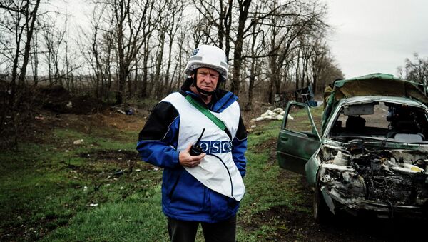 An International observer of the Organization for Security and Co-operation in Europe (OSCE) stands next to a destroyed car after shelling during an inspection tour near the village of Shirokino, near the eastern Ukrainian port city of Mariupol - Sputnik International