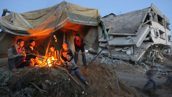 Palestinians sit around a fire under the cover of a tent on the ruins of their home - Sputnik International