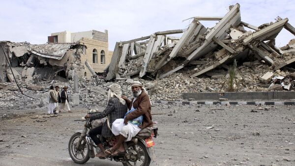 People ride on a motorcycle as they pass by a police headquarters destroyed by a Saudi-led air strike in Yemen's northwestern city of Saada May 7, 2015 - Sputnik International