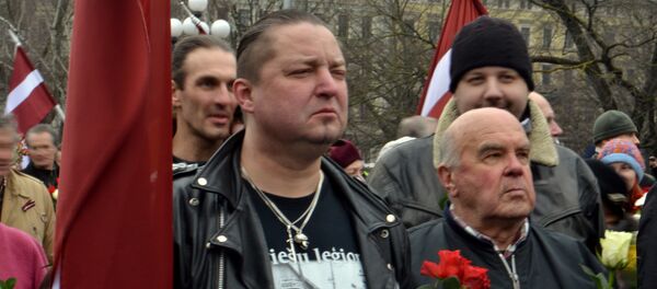 The shirt this man is wearing has written Latvian Legion..., an a picture of a Nazi tank with the Latvian Legion badge at the bottom right. The shirt this man is wearing has written Latvian Legion..., an a picture of a Nazi tank with the Latvian Legion badge at the bottom right. - Sputnik International