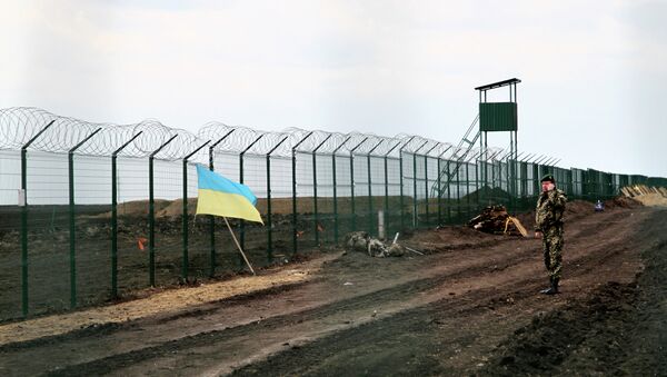 A Ukrainian border guard officer speaks on a phone near a national flag attached to the fence on the Ukrainian-Russian border near Hoptivka, Kharkiv region, eastern Ukraine - Sputnik International