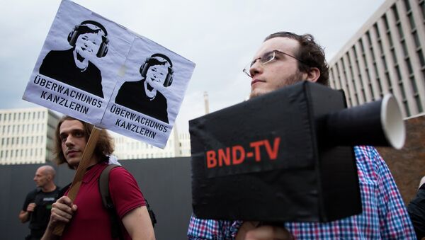 Demonstrators hold a poster showing a portrait of German Chancellor Angela Merkel reading surveillance Chancellor and a fake surveillance camera during a protest against the surveillance by the US National Security Agency, NSA. - Sputnik International